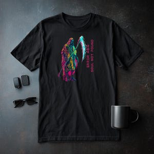 May include: Black t-shirt featuring a colorful graphic of the Grim Reaper with a scythe. The text "ERROR 404: SOUL NOT FOUND" is printed vertically on the right side. Sunglasses, a mug, and other items are on a dark surface.