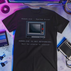 May include: Black t-shirt with a retro computer monitor graphic. The text on the shirt reads "Human.exe - System Error" and "HUMAN.EXE IS NOT RESPONDING. Wait for program to respond?"
