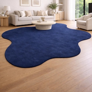 Op de afbeelding: Een marineblauwe vloerkleed met een organische vorm ligt op een lichte houten vloer. Het vloerkleed contrasteert met de neutrale meubels in de woonkamer en geeft de ruimte een moderne uitstraling.