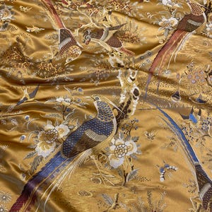 May include: A golden satin fabric featuring an intricate embroidered pattern of long-tailed birds, including pheasants, interspersed with detailed floral motifs and branches. The embroidery uses shades of blue, brown, white, and red thread.