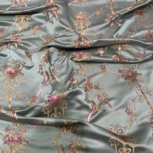 May include: Silky, sage green fabric with a repeating pattern of ornate gold candelabras, birds, and floral elements in shades of pink and burgundy. The fabric has a subtle sheen, suggesting a luxurious material suitable for apparel or home decor.