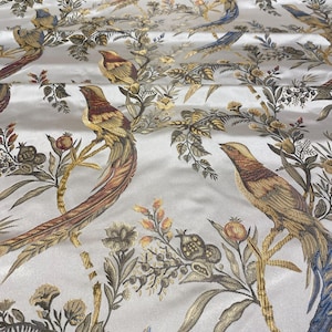 May include: A white satin fabric featuring an intricate print of long-tailed birds perched on branches with detailed leaves, flowers, and pomegranate-like fruits in shades of gold, brown, blue, and muted green throughout the repeating pattern.