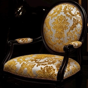 Könnte beinhalten: Ein verzierter Sessel mit einem dunklen Holzrahmen und gold-silber gemusterten Polstern. Rückenlehne und Sitzfläche weisen ein detailliertes Blumenmuster auf, und auch die Armlehnen sind gepolstert. Der Stuhl hat eine luxuriöse, Vintage-Ästhetik.