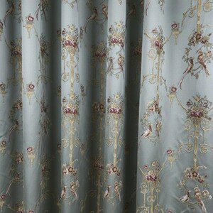 May include: Pale blue curtain fabric with a repeating pattern of birds, flowers, and ornate gold-colored scrollwork. The fabric has a silky sheen and a classic, elegant design, suitable for home decor.