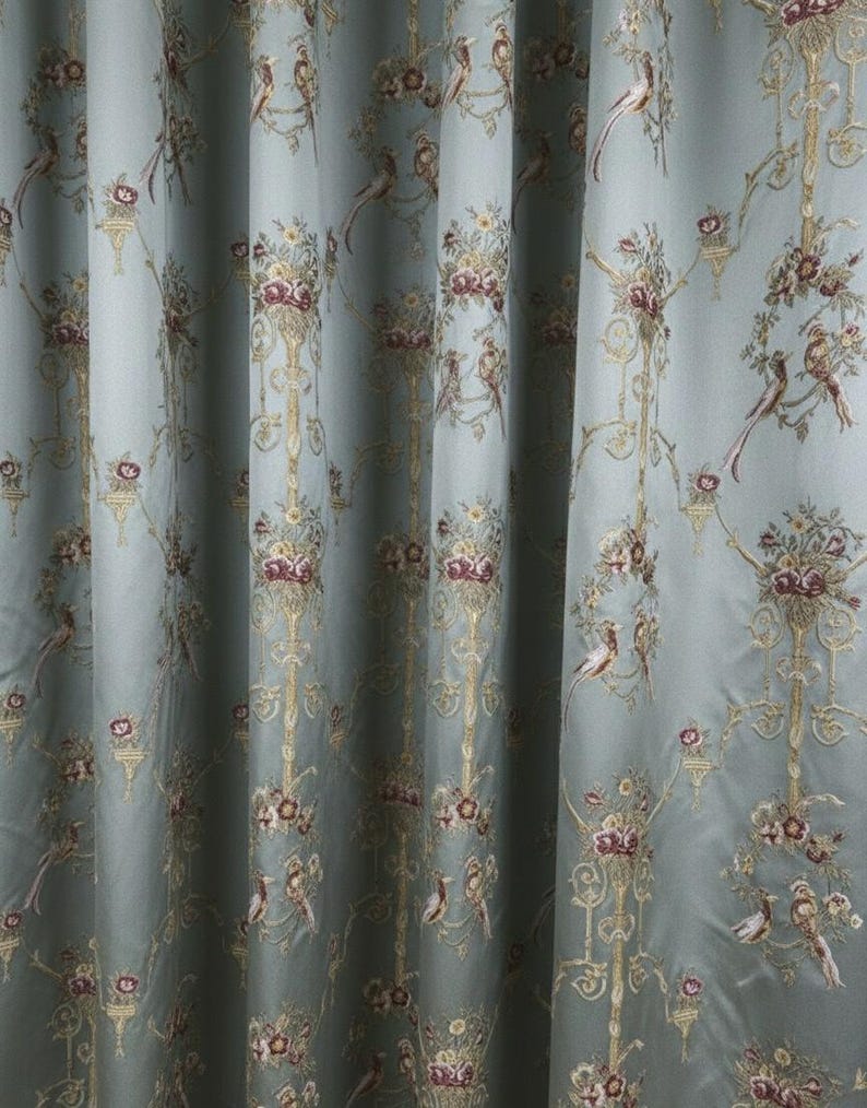 May include: Pale blue curtain fabric with a repeating pattern of birds, flowers, and ornate gold-colored scrollwork. The fabric has a silky sheen and a classic, elegant design, suitable for home decor.