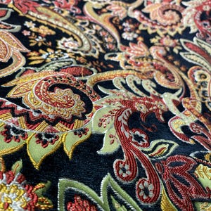 Può includere: Un tessuto nero caratterizzato da un intricato motivo paisley multicolore, ricamato con fili dorati metallizzati, rosso intenso e verde salvia. Il design è composto da forme a goccia vorticose, motivi floreali ed elementi botanici.