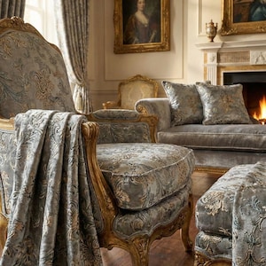 May include: An ornate living room set featuring a patterned gray and gold fabric. The set includes an armchair, a chaise lounge, and a footstool, all with carved wooden frames. The room also features a fireplace, paintings, and draped curtains.