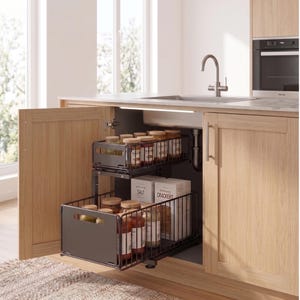Può includere: Un mobile da cucina con cestelli estraibili in filo metallico pieni di barattoli di spezie e condimenti. Il mobile è in legno chiaro e ha un lavello e un rubinetto in acciaio inossidabile. I cestelli sono grigio scuro.