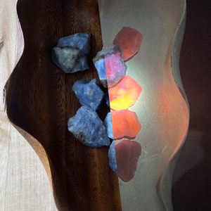 May include: A wooden bowl filled with blue and red gemstones. The bowl is on a light wood surface. The background is black.