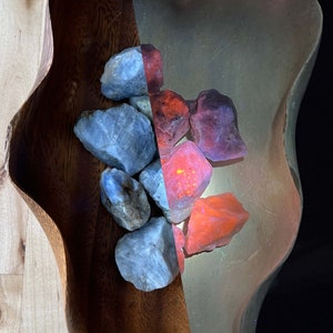 May include: A wooden bowl filled with smooth, gray stones and red, orange, and pink stones. The bowl is on a light wood surface.