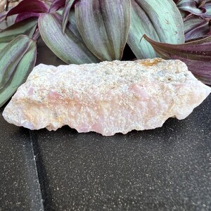 May include: A large, rough, pink and white crystal with a natural, irregular shape. The crystal has a smooth, polished surface and is sitting on a black background.