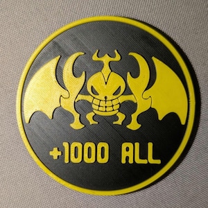 May include: A round, black and yellow emblem featuring a stylized yellow creature with wings and the text "+1000 ALL". The emblem has a textured surface and a yellow border.