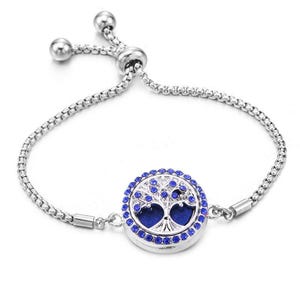 May include: Silver bracelet with a round pendant depicting a tree of life. The pendant is surrounded by blue crystals and has a dark blue centre. The bracelet features an adjustable sliding clasp.