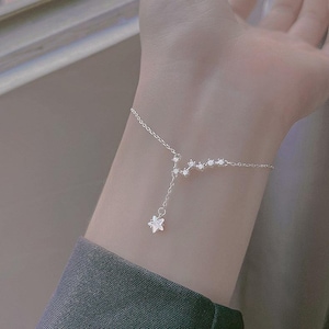 May include: A delicate silver bracelet featuring a constellation design with sparkling crystals. A small star charm dangles from the bracelet. The bracelet is worn on a wrist, against a soft background.