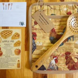 May include: A kitchen gift set featuring a quilted potholder with a rooster print, a wooden slotted spoon, a blank recipe card, and an apple pie recipe card. The brown paper tag attached to the potholder reads BeezMountainBoutique Housewarming Gift Set.
