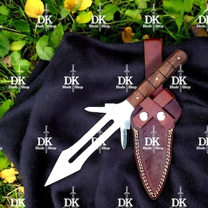 May include: A handmade knife with a wooden handle and a stainless steel blade, presented with a brown leather sheath. The knife features a unique design with a secondary blade. The sheath has decorative stitching and the text "DK Blade Shop".