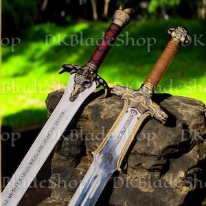 K&ouml;nnte beinhalten: Zwei dekorative Schwerter mit verzierten Griffen und Klingen. Ein Schwert hat einen rot umwickelten Griff und das andere einen braun umwickelten Griff. Die Klingen haben ge&auml;tzte Designs und Text. Die Schwerter liegen auf einem Felsen.