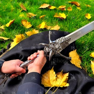 May include: A silver fantasy sword with a detailed dragon head hilt and a wide blade. The sword is held against a backdrop of green grass and fallen yellow leaves. The text "DK Blade Shop" is visible.