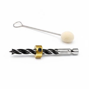 May include: A set of woodworking tools, including a black and silver drill bit with a gold-colored collar, a silver metal tool, and a small, off-white felt ball. The tools are set against a white background.