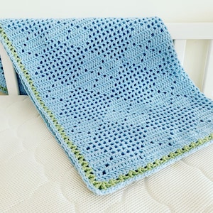 May include: A light blue crocheted baby blanket with a green border. The blanket is made with a simple stitch pattern and is soft and cozy.