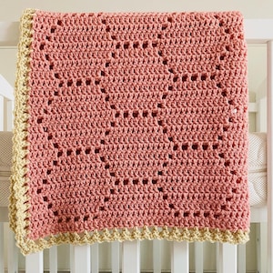 Puede incluir: Una manta de bebé de ganchillo en color rosa polvoriento con un borde de ganchillo amarillo. La manta está hecha con un patrón de punto de diamante.