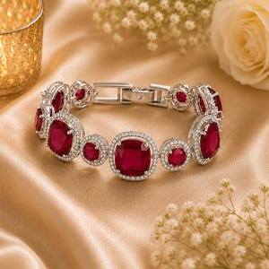 May include: A silver-toned link bracelet featuring alternating large and small cushion-cut deep red gemstones. Each stone is surrounded by a halo of small clear pavé crystals. The bracelet includes a secure metal clasp mechanism for closure.
