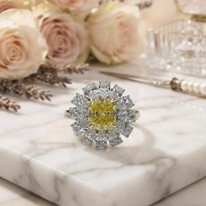Puede incluir: Un anillo con una piedra central amarilla de corte cojín rodeada por un doble halo de pequeñas piedras blancas transparentes de corte redondo dispuestas en forma floral, montado sobre una banda de metal pulido con acabado brillante.