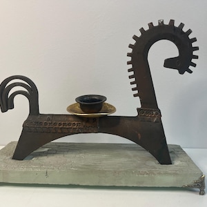May include: A unique, handcrafted metal sculpture in the shape of a horse. The dark brown sculpture features a small cup on a gold-colored plate. The horse is mounted on a rectangular base with decorative metal feet.