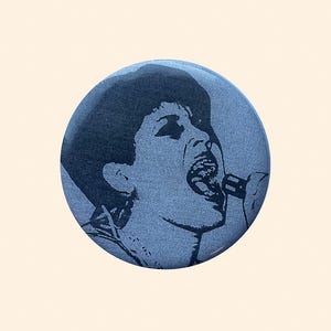 Puede incluir: Un botón redondo azul con una ilustración en blanco y negro de una persona cantando a un micrófono. La imagen es un retrato estilizado con una apariencia texturizada, sobre un fondo claro.