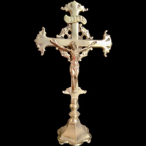 May include: A gold-toned crucifix featuring a detailed representation of Jesus Christ. The cross has decorative, ornate arms and a base. The letters INRI are displayed above the figure.