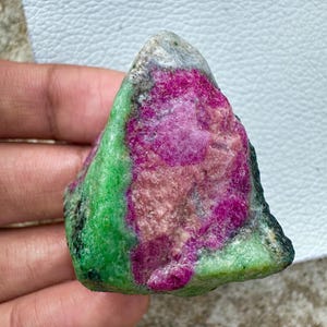 Op de afbeelding: Een ruw geslepen edelsteen met een levendige kleurenpracht. De steen heeft een opvallende combinatie van diep magenta, lichtroze en heldergroene tinten. Het natuurlijke, ongepolijste oppervlak draagt bij aan de unieke uitstraling.