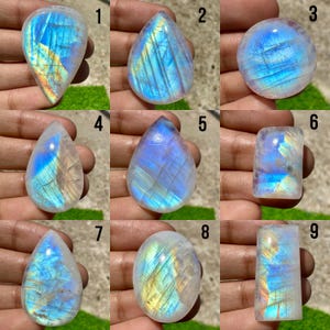 May include: Nine polished moonstone gemstones in various shapes. The stones display a range of colors, including blue, white, and yellow, with a shimmering, iridescent effect. The shapes include teardrops, ovals, and a round stone, each with unique internal patterns.