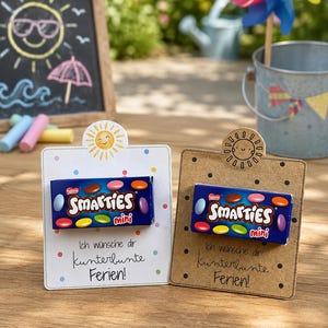 Könnte beinhalten: Zwei rechteckige Karten mit einer kleinen Schachtel Smarties mini in der Mitte. Eine Karte ist weiß mit bunten Punkten und einem Sonnen-Symbol, die andere braun mit schwarzen Punkten und einer Sonne. Beide tragen den Text Ich wünsche dir kunterbunte Ferien!