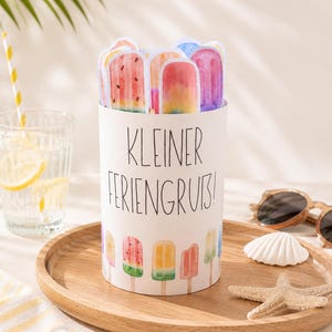 May include: A cylindrical white paper container featuring the black text KLEINER FERIENGRUB! and a colorful watercolor illustration of various popsicles at the base, with several die-cut popsicle paper cutouts extending from the top opening.