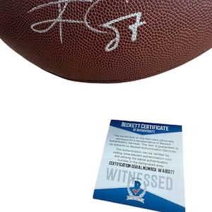 May include: A brown football with a white signature. A Beckett Certificate of Authenticity is included, with the text "WITNESSED" and certification serial number W A85577.
