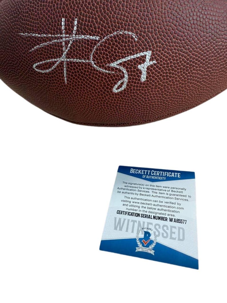 May include: A brown football with a white signature. A Beckett Certificate of Authenticity is included, with the text "WITNESSED" and certification serial number W A85577.