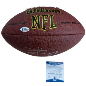May include: A brown Wilson NFL football with white laces and gold lettering. The football has a signature and a Beckett authentication sticker. A Beckett Certificate of Authenticity is below the football.