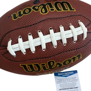 May include: A brown leather Wilson football with white laces. The football has the Wilson logo in gold lettering. A Beckett Certificate of Authenticity is included.