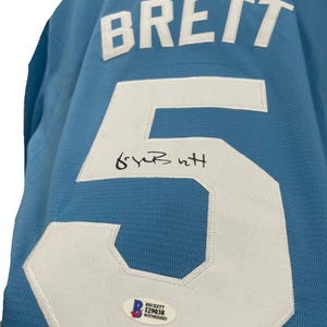 May include: Light blue jersey with the name "BRETT" in white block letters and the number "5" in white. The jersey has an autograph and a Beckett authentication sticker.