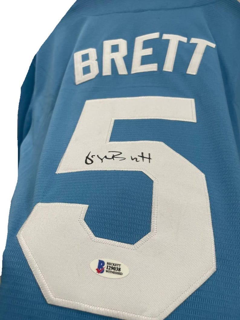 May include: Light blue jersey with the name "BRETT" in white block letters and the number "5" in white. The jersey has an autograph and a Beckett authentication sticker.