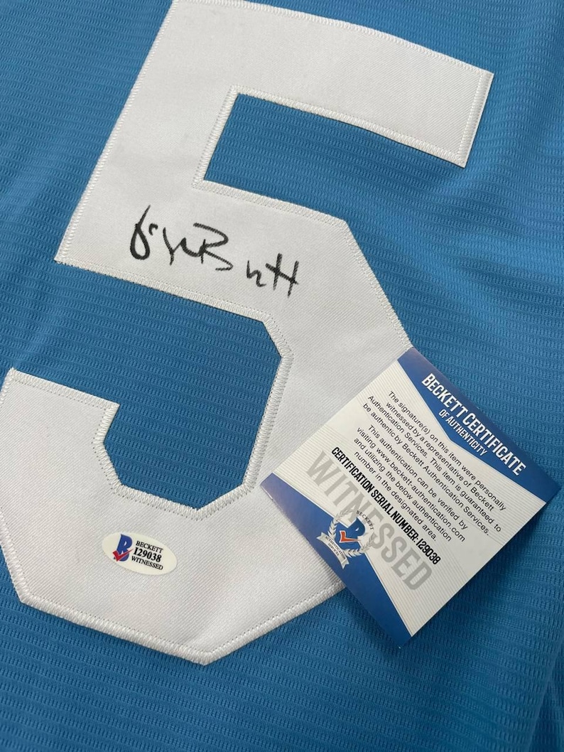 May include: Light blue jersey with a large white number 5 patch. The number is stitched onto the jersey. The jersey has a signature and a Beckett Certificate of Authenticity with the certification serial number 129038.