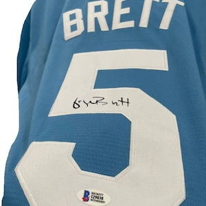 May include: Light blue jersey with the name "BRETT" in white block letters across the back. A large white number "5" is prominently displayed, with a signature above it. A Beckett authentication sticker is visible.