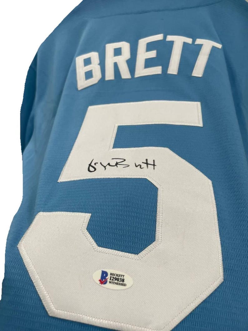 May include: Light blue jersey with the name "BRETT" in white block letters across the back. A large white number "5" is prominently displayed, with a signature above it. A Beckett authentication sticker is visible.