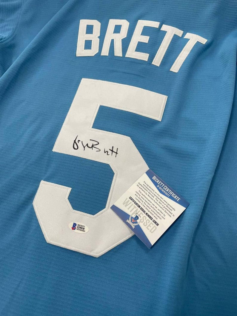 May include: Light blue jersey with the name "BRETT" in white letters across the top. A large white number "5" is sewn on the front, with a signature below. A Beckett Certificate of Authenticity is attached.