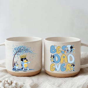 May include: Two ceramic mugs with a cream-colored body and a brown base. One mug features a cartoon dog with a crown and the text "Daddy" and "Lottie". The other mug says "Best Dad Ever" with cartoon dog illustrations.