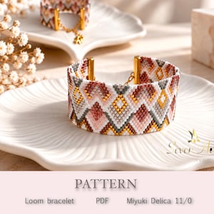 May include: A woven loom bracelet featuring a geometric diamond pattern in shades of white, dusty pink, grey, and metallic gold. The bracelet is finished with gold-toned metal end bars and a delicate chain clasp, showcasing intricate beadwork.