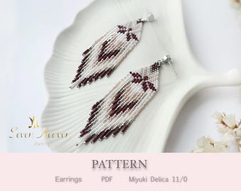 May include: A pair of handmade beaded earrings in a feather design. The earrings feature a combination of white, light pink, and burgundy beads, with silver-colored ear posts. The earrings are displayed on a white, decorative plate.