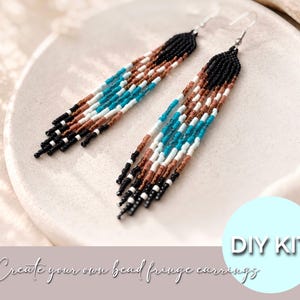 Op de afbeelding: Een paar lange franjeoorbellen gemaakt van kleine kraaltjes in een kleurenpalet van zwart, bruin, wit en turquoise. De oorbellen hebben een driehoekig bovengedeelte dat overgaat in meerdere hangende strengen van kralen. DIY KIT.
