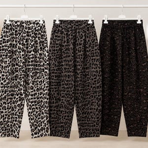 Könnte beinhalten: Drei Hosen hängen an einem weißen Kleiderständer, jede mit einem unterschiedlichen Leopardenmuster. Das erste Paar ist weiß mit schwarzen Flecken, das zweite grau mit schwarzen Flecken und das dritte schwarz mit dunkelbraunen Leopardenflecken.