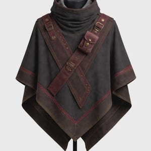 May include: A dark grey poncho with a high collar and a brown leather harness. The harness has a small pouch and is secured with buckles. The edges of the poncho are trimmed with brown leather and a thin red stripe.